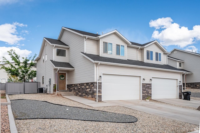 view of front of house with a garage, driveway, fence, stone siding, and central AC unit