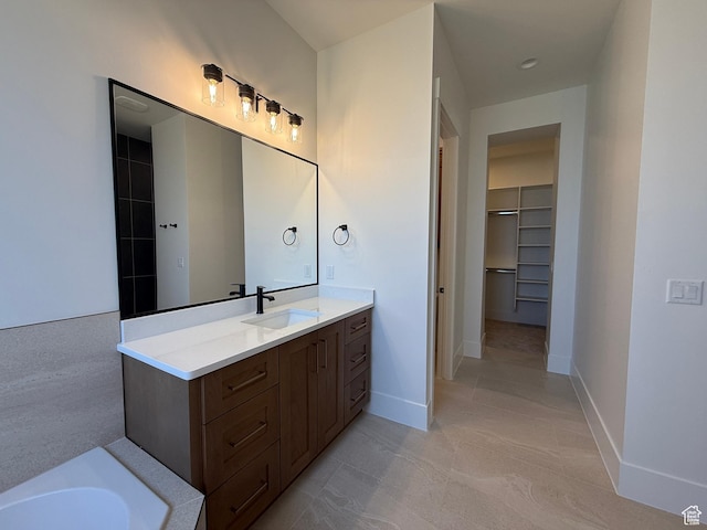 bathroom with a walk in closet, vanity, baseboards, and a bath