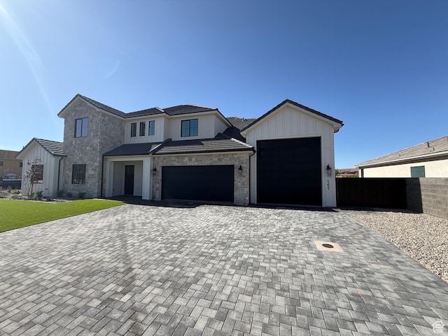 view of front facade featuring stone siding, decorative driveway, fence, and a garage