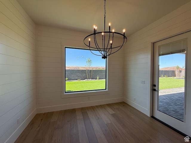 unfurnished dining area with a chandelier, wood finished floors, healthy amount of natural light, and baseboards