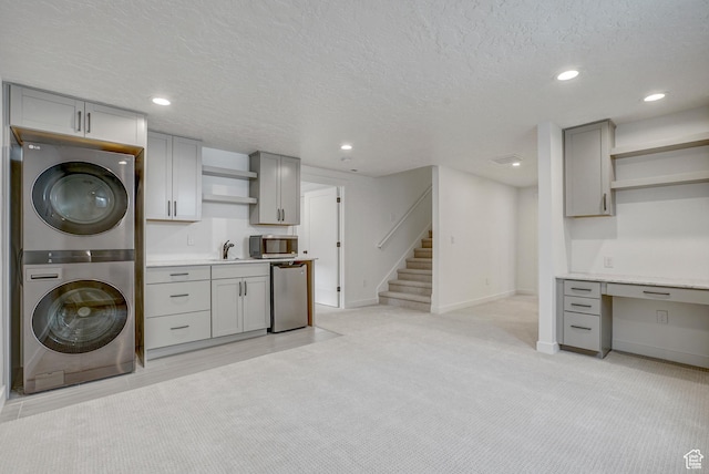 clothes washing area featuring stacked washing machine and dryer, a textured ceiling, baseboards, recessed lighting, and light carpet