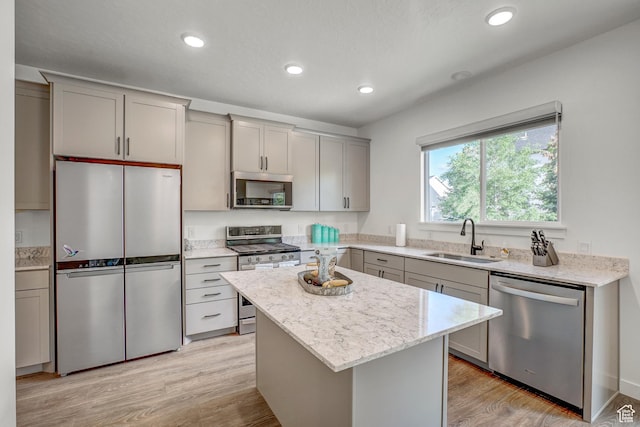 kitchen featuring stainless steel appliances, a sink, gray cabinetry, light wood-style flooring, and a center island
