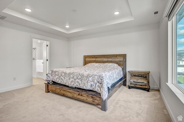 bedroom with light carpet, recessed lighting, a tray ceiling, baseboards, and connected bathroom