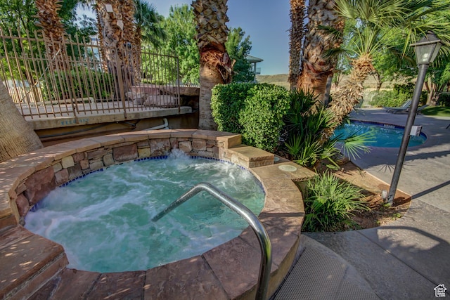 view of pool featuring an in-ground hot tub and fence