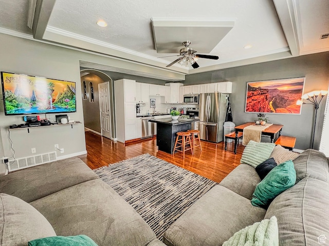living area with wood finished floors, arched walkways, ceiling fan, recessed lighting, and crown molding