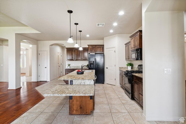 417 E Stonehedge Cir, Washington, UT 84780 - kitchen featuring black appliances, arched walkways, a breakfast bar area, an island with sink, and light stone countertops
