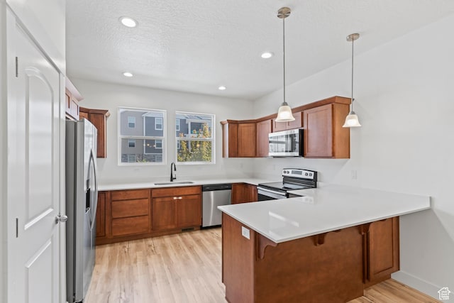 kitchen with appliances with stainless steel finishes, a sink, a peninsula, brown cabinetry, and light wood finished floors
