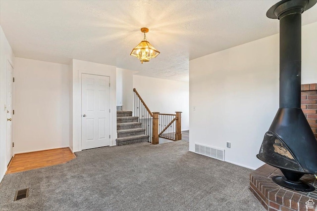unfurnished living room featuring a wood stove, carpet, a chandelier, stairs, and a textured ceiling