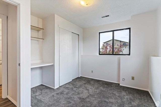unfurnished bedroom featuring dark colored carpet, a textured ceiling, a closet, and baseboards