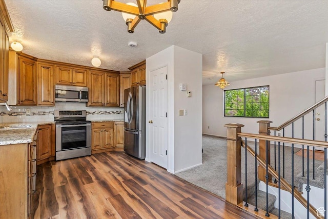 kitchen with stainless steel appliances, brown cabinetry, dark wood-style floors, a textured ceiling, and a sink