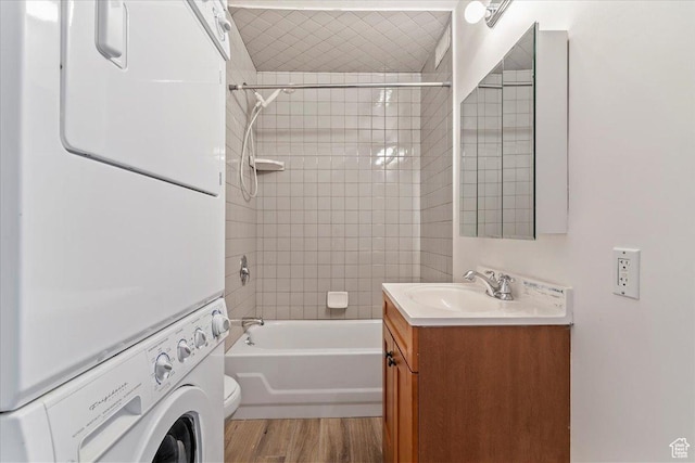 bathroom featuring stacked washer and clothes dryer, wood finished floors, tub / shower combination, vanity, and toilet