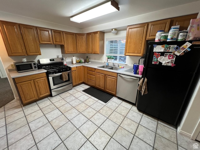 kitchen featuring appliances with stainless steel finishes, a sink, light countertops, and brown cabinets