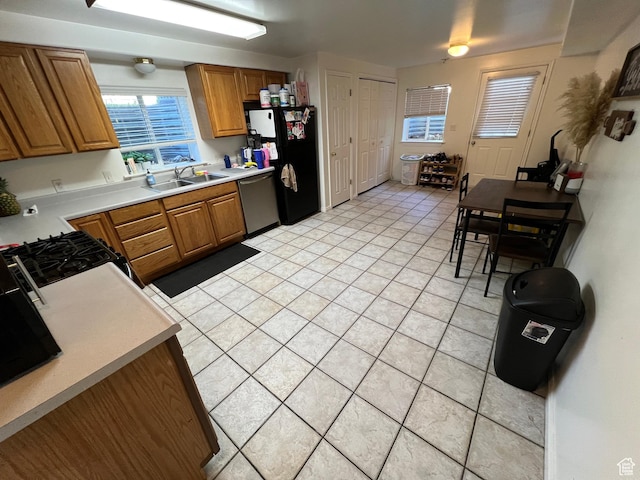 kitchen with freestanding refrigerator, stainless steel dishwasher, a sink, and brown cabinetry
