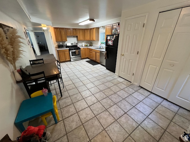 kitchen featuring stainless steel appliances, a sink, light countertops, light tile patterned floors, and brown cabinets