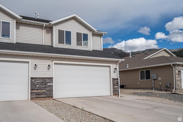 view of front of property featuring stone siding, concrete driveway, a garage, and a mountain view
