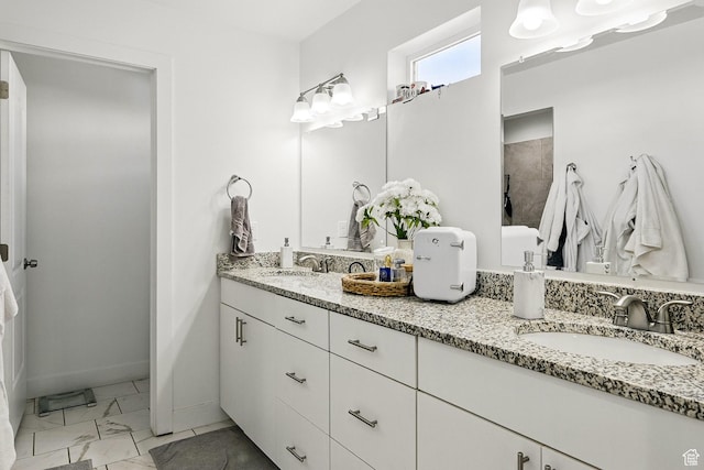 bathroom featuring marble look tile flooring, double vanity, tiled shower, and baseboards