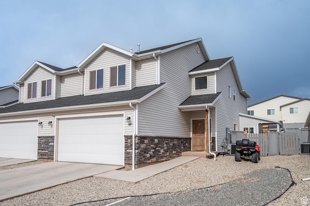 view of front facade with stone siding, driveway, a garage, fence, and cooling unit