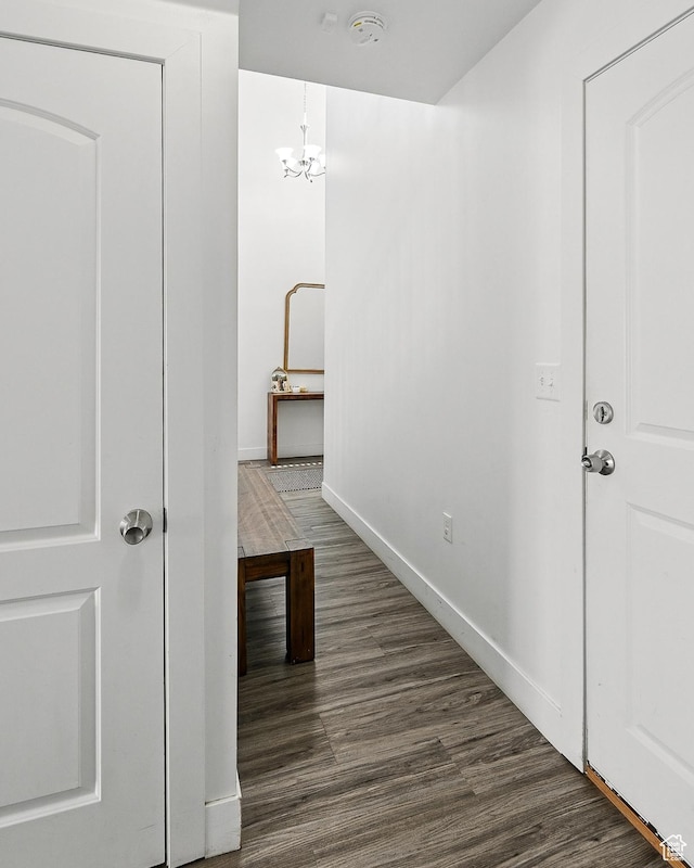 corridor featuring dark wood-type flooring, baseboards, and a chandelier