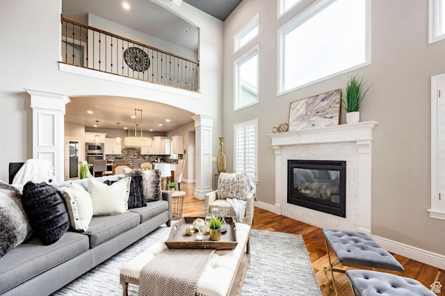 1309 W Atrium Ct W, Farmington, UT 84025 - living area featuring decorative columns, a towering ceiling, a glass covered fireplace, light wood finished floors, and baseboards