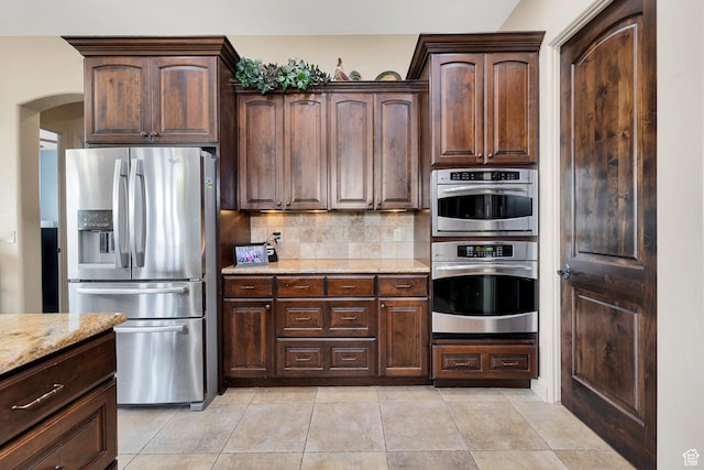 373 W Meridian Dr, Ivins, UT 84738 - kitchen featuring stainless steel fridge with ice dispenser, light stone countertops, decorative backsplash, arched walkways, and dark brown cabinetry