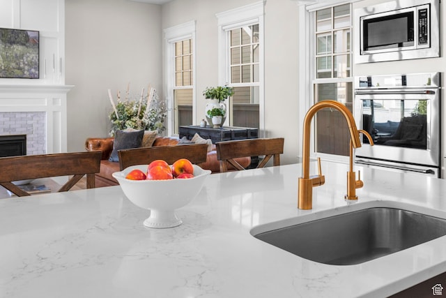 kitchen view of appliances with stainless steel finishes, a sink, a fireplace, and light stone countertops