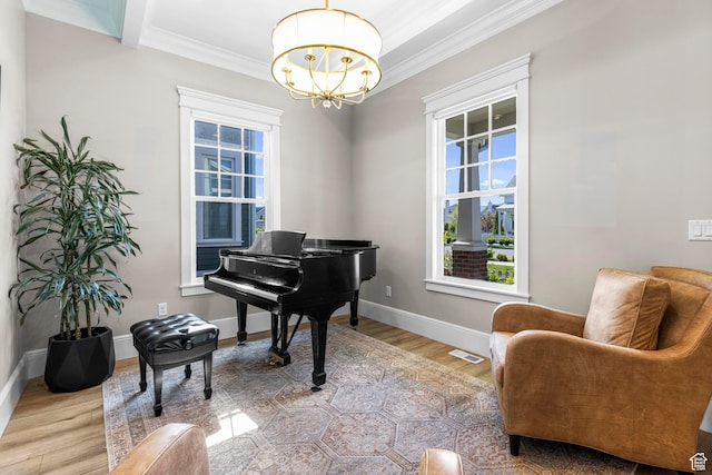 sitting room with a chandelier, crown molding, healthy amount of natural light, wood finished floors, and baseboards