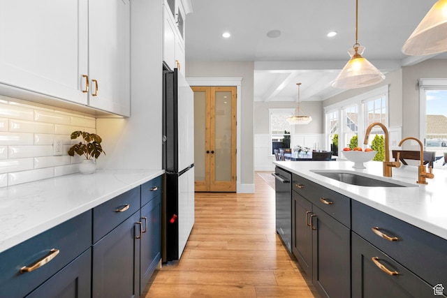kitchen featuring a sink, light wood finished floors, white cabinets, freestanding refrigerator, and decorative light fixtures