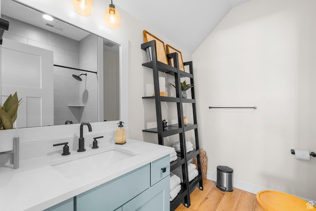 full bath with wood finished floors, a tile shower, vaulted ceiling, vanity, and baseboards