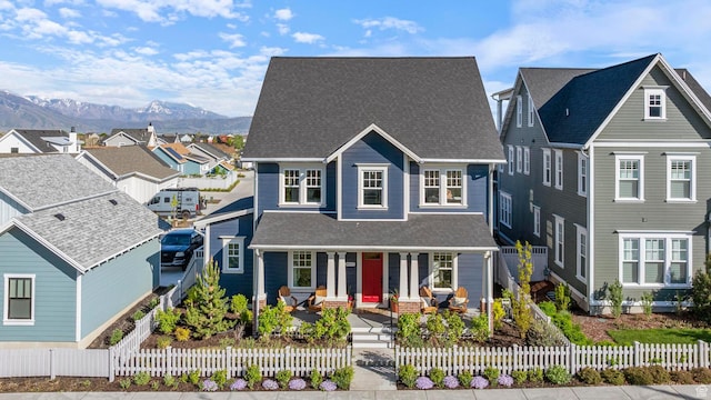 view of front facade with a porch, a mountain view, roof with shingles, a residential view, and a fenced front yard