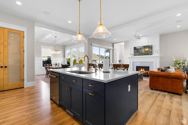 kitchen featuring a sink, open floor plan, a glass covered fireplace, light wood-type flooring, and light countertops