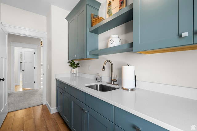 kitchen with open shelves, a sink, wood finished floors, light countertops, and baseboards