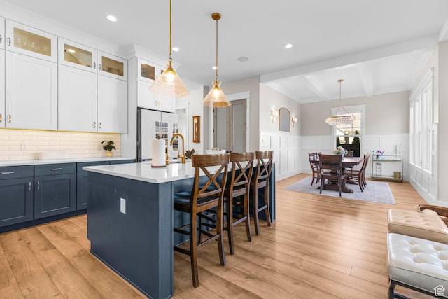 kitchen featuring white fridge, beam ceiling, light wood-type flooring, light countertops, and wainscoting