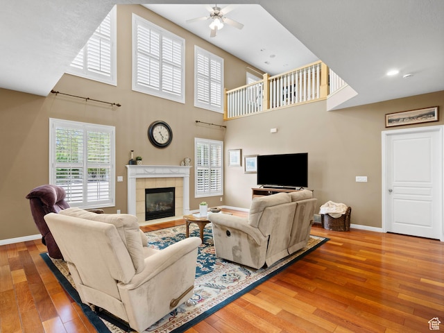living room with a ceiling fan, hardwood / wood-style floors, baseboards, a fireplace, and a towering ceiling