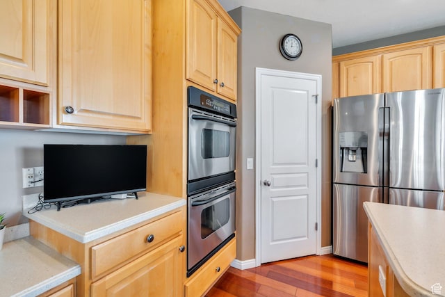 kitchen featuring stainless steel fridge, light brown cabinets, double oven, and light wood-type flooring