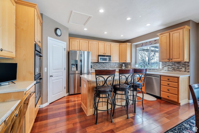 kitchen with appliances with stainless steel finishes, light brown cabinetry, a kitchen bar, wood finished floors, and recessed lighting