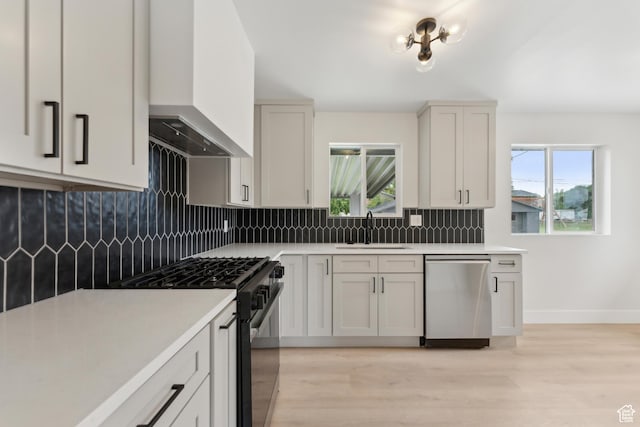 kitchen with stainless steel dishwasher, black gas stove, a sink, wall chimney exhaust hood, and light countertops