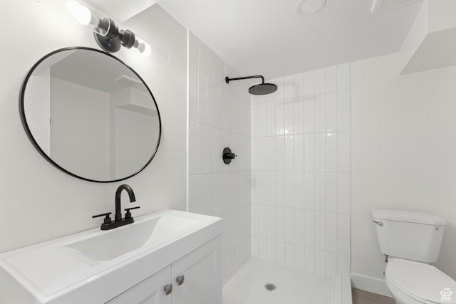bathroom with a tile shower, toilet, and vanity