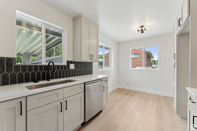 kitchen with dishwasher, a sink, decorative backsplash, light wood-type flooring, and light countertops
