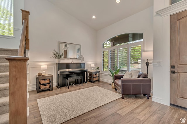 living area with a decorative wall, stairs, high vaulted ceiling, wood finished floors, and recessed lighting