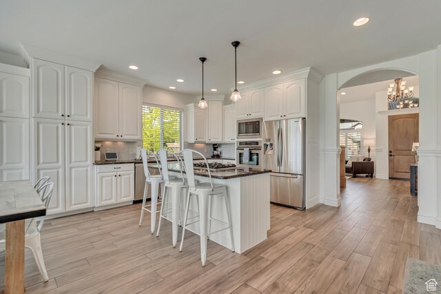 kitchen with appliances with stainless steel finishes, arched walkways, light wood-style floors, white cabinetry, and a kitchen bar