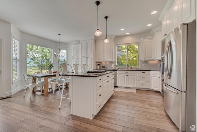 kitchen featuring stainless steel appliances, white cabinetry, a breakfast bar, a center island, and backsplash