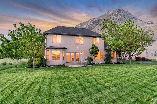 back of house featuring stucco siding, a yard, and a mountain view
