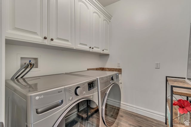 washroom featuring washing machine and dryer, cabinet space, baseboards, and wood finished floors