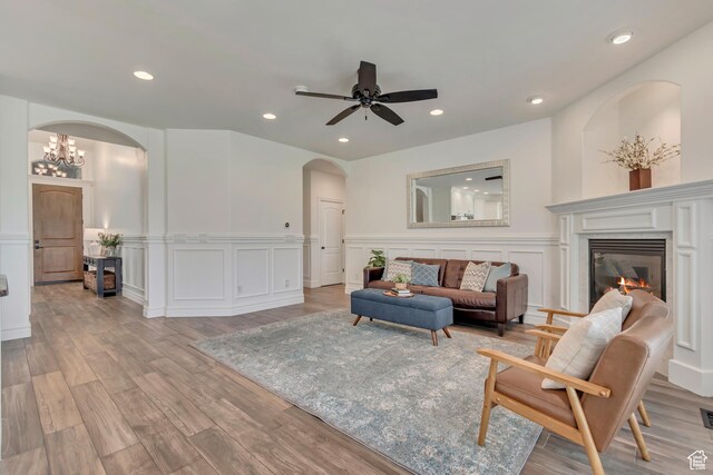 living room featuring arched walkways, a decorative wall, light wood-style flooring, recessed lighting, and wainscoting