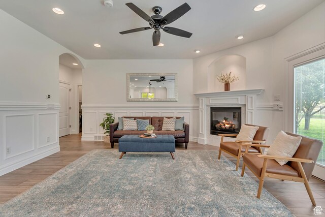 living room featuring a decorative wall, light wood-style floors, a glass covered fireplace, recessed lighting, and a ceiling fan