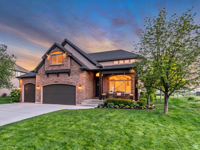 view of front facade featuring a yard, concrete driveway, stone siding, covered porch, and a garage