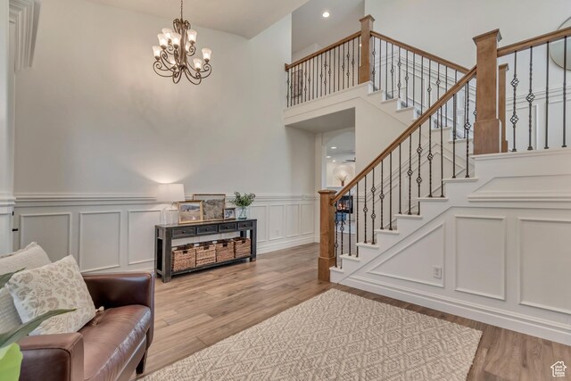 living area with stairway, wood finished floors, a decorative wall, a chandelier, and a wainscoted wall