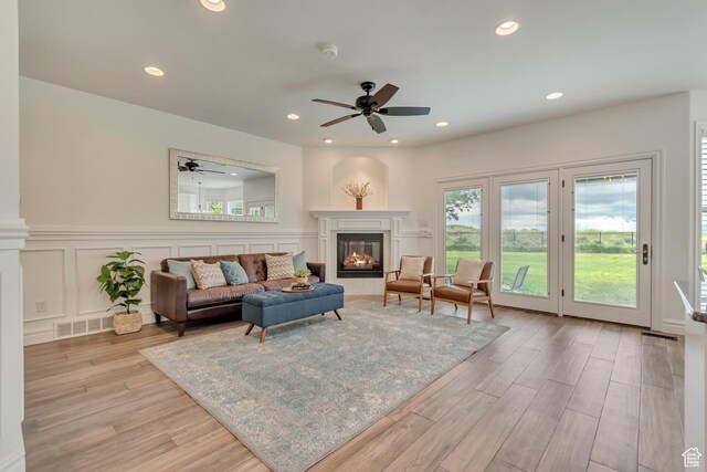 living room with a ceiling fan, a glass covered fireplace, light wood-style flooring, recessed lighting, and a decorative wall