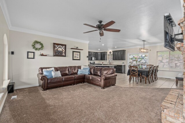 living room featuring a ceiling fan, ornamental molding, baseboards, light carpet, and light tile patterned floors