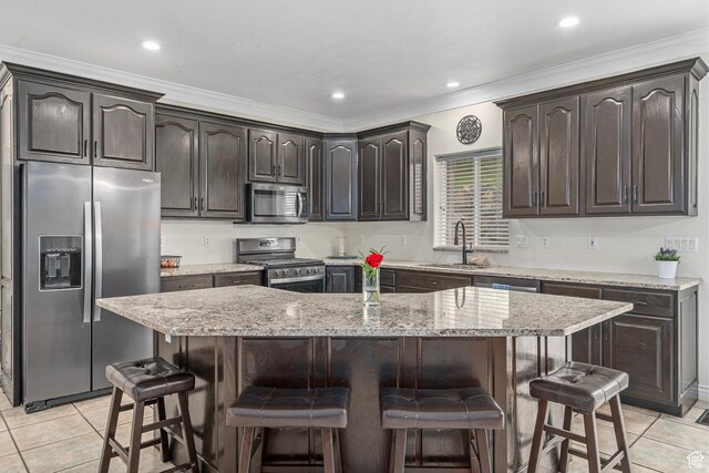 kitchen featuring appliances with stainless steel finishes, a sink, light tile patterned flooring, a breakfast bar, and crown molding